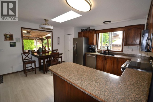 View of the kitchen with wood cabinets, granite island, stainless steel refrigerator, and outdoor view. - 3944 Trepanier Heights Avenue, Peachland