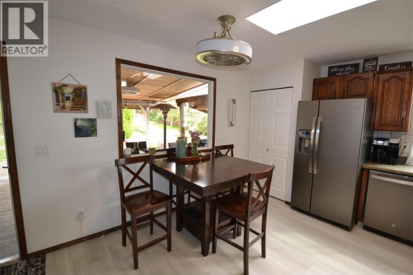 Kitchen dining area with a dark wood table, chairs, and a window overlooking the patio. - 3944 Trepanier Heights Avenue, Peachland