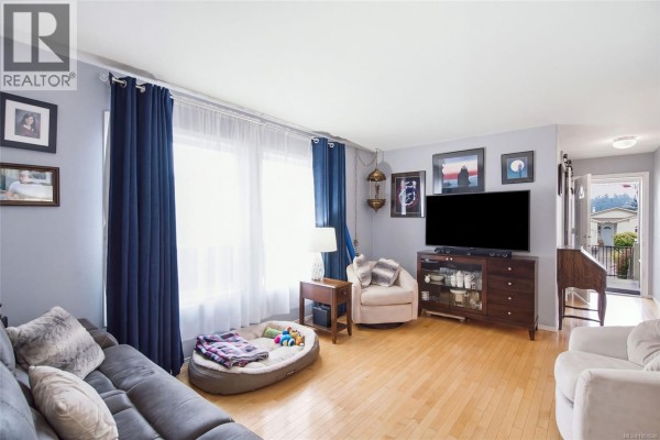 Living room with grey sofa, armchair, TV console, and entryway visible. - 3948 Valewood Dr, Nanaimo