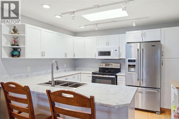Modern kitchen with white cabinets, stainless steel appliances, and marble countertops. - 3948 Valewood Dr, Nanaimo