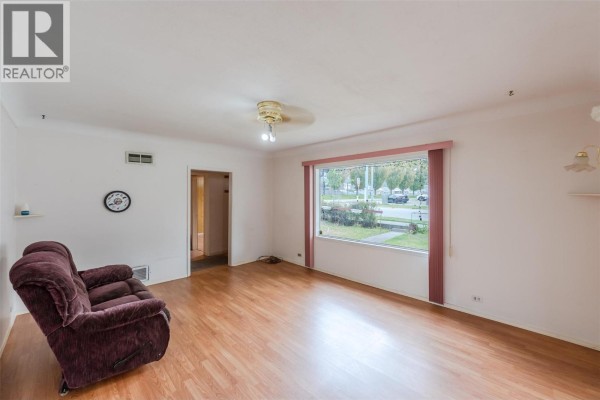 Living room with light wood laminate flooring, white walls, and a large picture window. - 395 Edmonton Avenue, Penticton