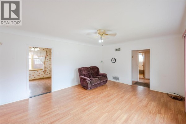 Living room with light wood laminate flooring, white walls, and an opening to another room. - 395 Edmonton Avenue, Penticton