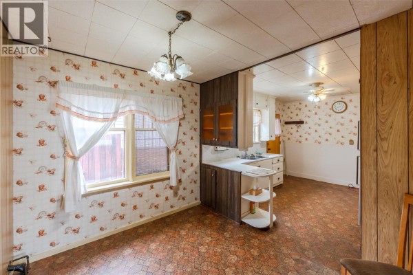 Dining area with orange patterned wallpaper, a window with white curtains, and dark wood cabinets. - 395 Edmonton Avenue, Penticton