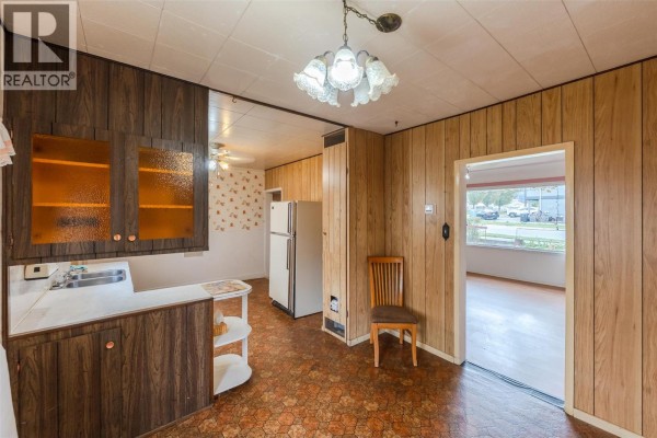 Kitchen with wood paneling, a double sink, white refrigerator, and an opening to another room. - 395 Edmonton Avenue, Penticton