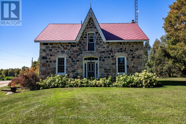 Front view of a stone farmhouse with a red metal roof and decorative gable trim. - 395 Elsinore Road N, South Bruce Peninsula