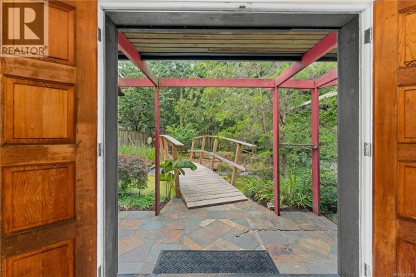 View from inside looking out through double doors to a covered entryway with a wooden bridge and garden. - 395 Lyngail Pl, Gabriola Island