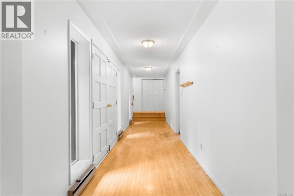 A long, bright hallway with white walls, hardwood floors, and multiple doors leading off. - 395 Lyngail Pl, Gabriola Island