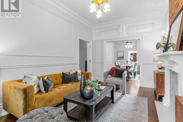Living room seating area with a gold sofa, grey chair, coffee table, and bay windows. - 395 Shaw Street, Toronto