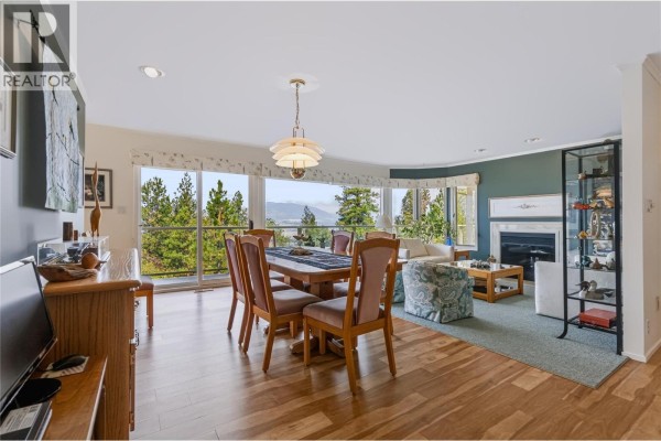Open-concept living and dining area with a fireplace and large windows with lake views. - 3954 Valleyview Road, Penticton