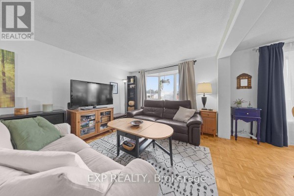 Living room with two sofas, coffee table, entertainment unit with television, and a large window. - 396 Hatfield Crescent, Ottawa