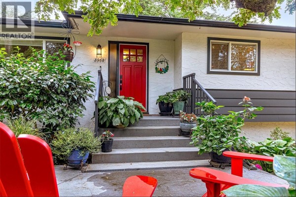 Front view of a white house with a gray horizontal siding and a red door. - 3960 Cumberland Rd, Saanich