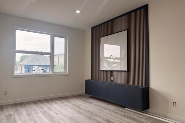 Living room with light wood-look flooring, white walls, and a large window. - 397 Kensington Street, Winnipeg