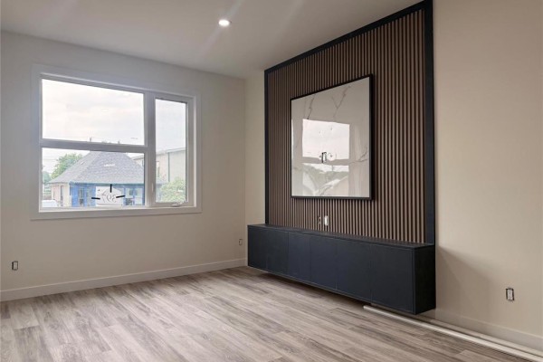 Unfurnished living room showcasing a large window and a wall-mounted entertainment unit. - 397 Kensington Street, Winnipeg