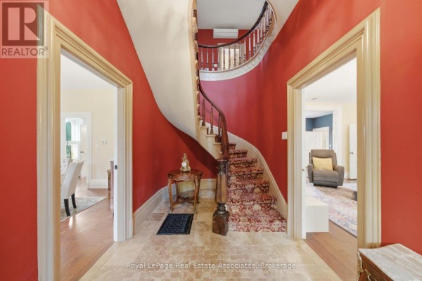 Grand foyer with red walls, a curving carpeted staircase, and arched doorways. - 398 Canboro Road, Pelham