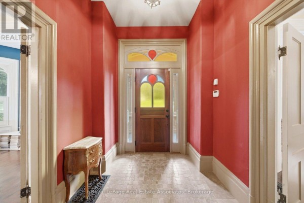 Entrance hallway with red walls, a wooden door with stained glass, and tiled floor. - 398 Canboro Road, Pelham