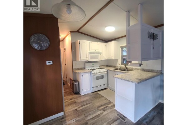 Kitchen view showing white cabinets, gas range, microwave, and a breakfast bar. - 3980 Squilax Anglemont Road Unit# 8, Scotch Creek