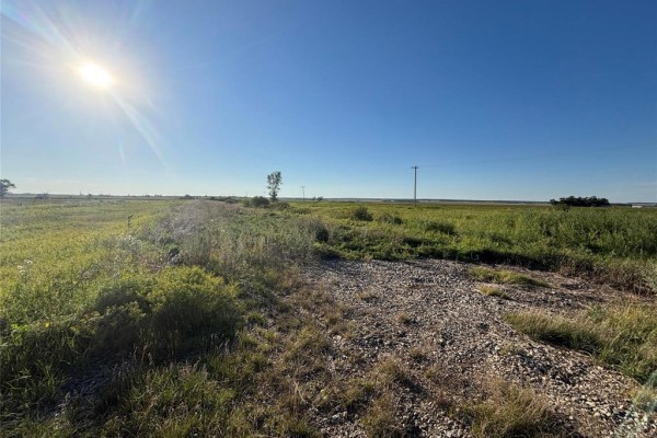 Aerial view of a long, narrow parcel of land highlighted in green, bordered by fields and a residential area. - 39800 Main Street, Nesbitt