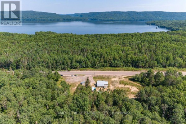 Aerial view of the house surrounded by trees, with a highway and lake in the distance. - 39869 Highway 17 Highway, Head, Clara And Maria