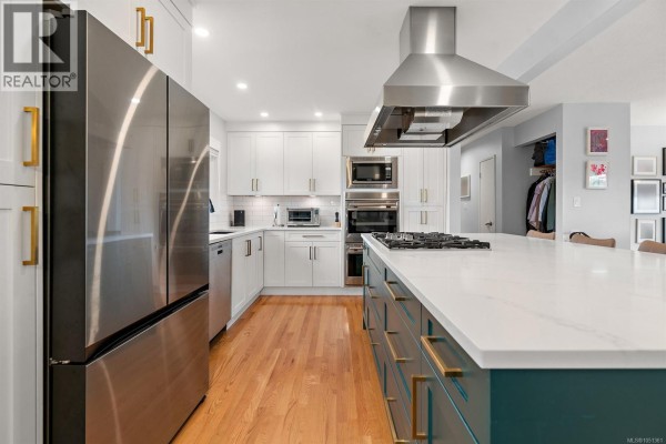 View of a spacious kitchen featuring white cabinetry, stainless steel refrigerator, and a large teal island. - 3988 Larchwood Dr, Saanich