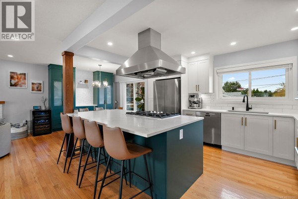 Kitchen island with seating for four and a gas stovetop, adjacent to a dining area with green cabinets. - 3988 Larchwood Dr, Saanich