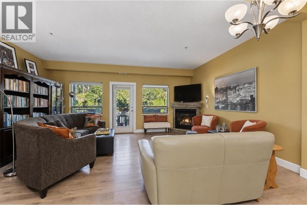 Living room with fireplace, bookshelves, sofa, chairs, and balcony door. - 3996 Beach Avenue Unit# 236, Peachland
