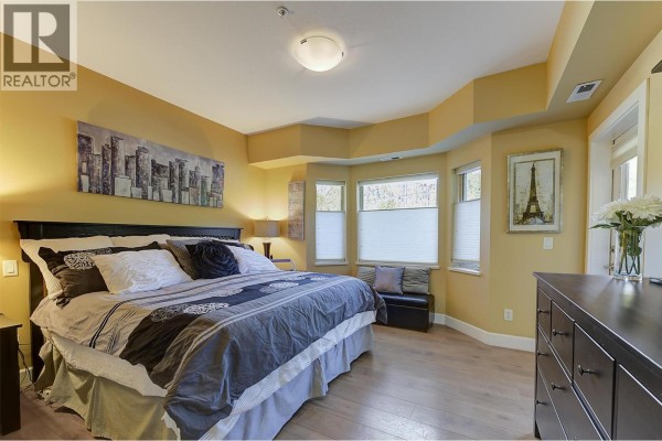 Bedroom with king-size bed, bay windows, dresser, and artwork. - 3996 Beach Avenue Unit# 236, Peachland