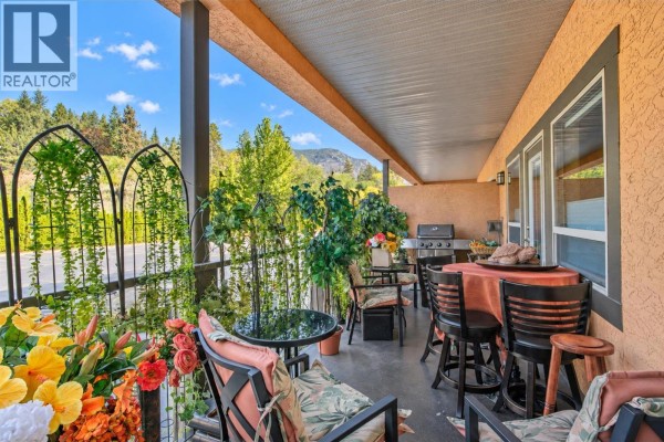 Covered patio with dining set, barbecue, and seating overlooking a garden area. - 3996 Beach Avenue Unit# 236, Peachland