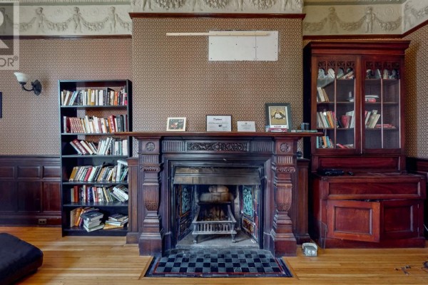 Close-up of a dark wood fireplace with intricate carvings and a tiled hearth, flanked by bookshelves. - 3a Forest Road, St  John S