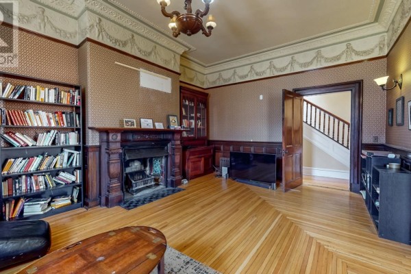 Living room with hardwood floors, a fireplace, bookshelves, and a doorway leading to a staircase. - 3a Forest Road, St  John S