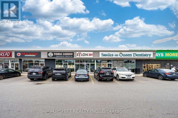 View of the commercial building from the parking lot, showing various businesses and parked cars. - 3b - 301 Queen Street S, Caledon
