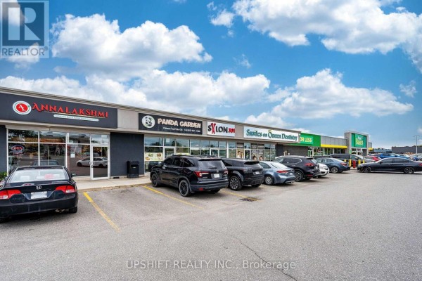 Wide shot of the commercial plaza with multiple businesses, parking lot, and cars under a cloudy sky. - 3b - 301 Queen Street S, Caledon