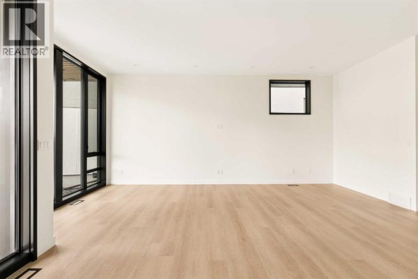 Empty living area with white walls, light wood floors, and large windows. - 3c Willow Crescent Sw, Calgary