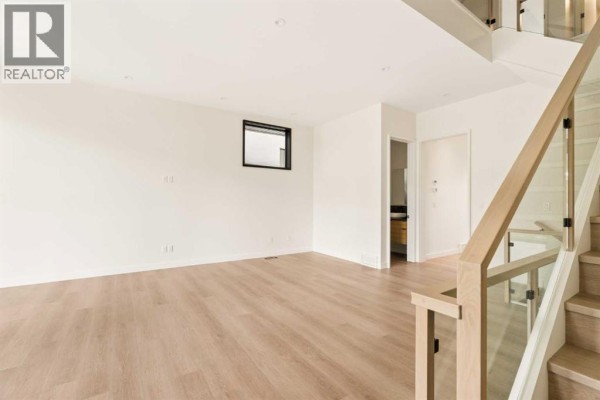 Empty room with white walls, light wood floors, and staircase. - 3c Willow Crescent Sw, Calgary