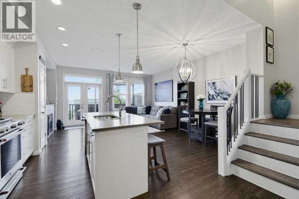 Open concept living area with kitchen island, dining table, and living room with large windows. - 3d Heritage Drive, Cochrane