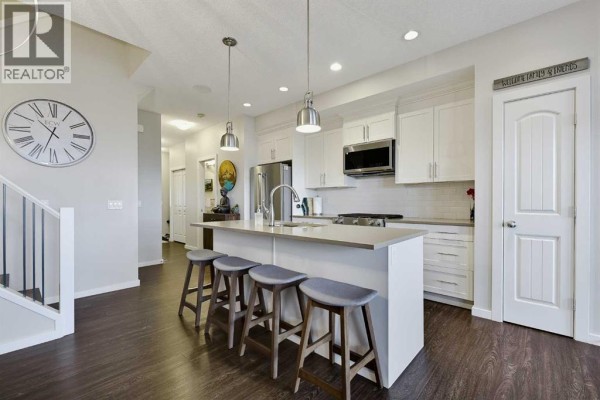 Modern kitchen with white cabinets, stainless steel appliances, and a large island with seating. - 3d Heritage Drive, Cochrane