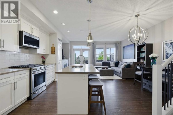 View of the open living space, including the kitchen island, dining area, and living room furniture. - 3d Heritage Drive, Cochrane