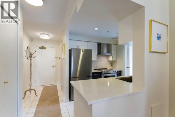 Kitchen area with stainless steel appliances, white cabinetry, and a breakfast bar. - 3f 199 Drake Street, Vancouver