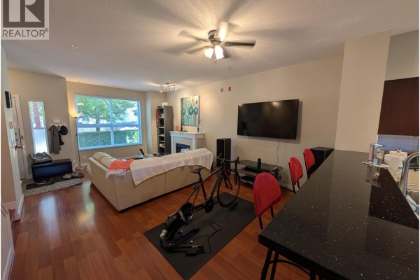 Living room with sofa, fireplace, television, stationary bicycle, kitchen island with bar stools and window view. - 3xxx E 54 Avenue, Vancouver