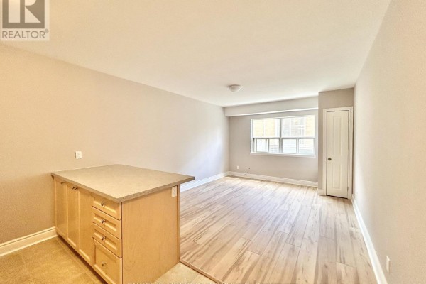 Living area with light wood floors, an island, and a large window. - 4 - 100 Twenty Fifth Street, Toronto