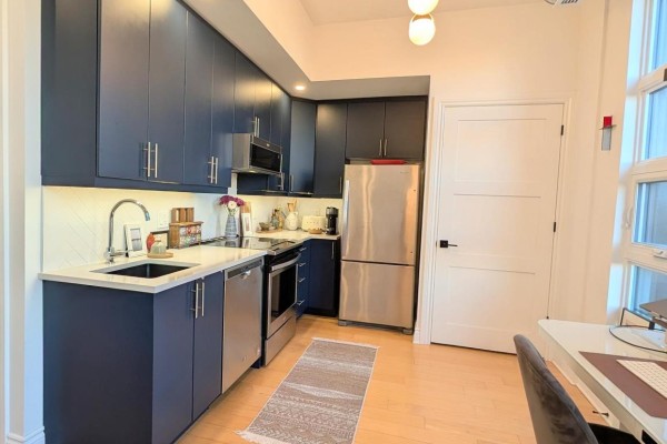 Modern kitchen with navy blue cabinets, stainless steel appliances, and a light wood floor. - 304 - 101 Pinhey Street, Ottawa
