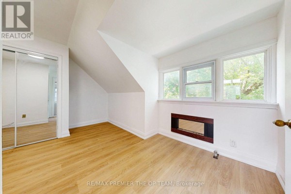 Attic bedroom with sloping ceilings, light wood floors, and three windows overlooking trees. - 4 - 11 Columbine Avenue, Toronto