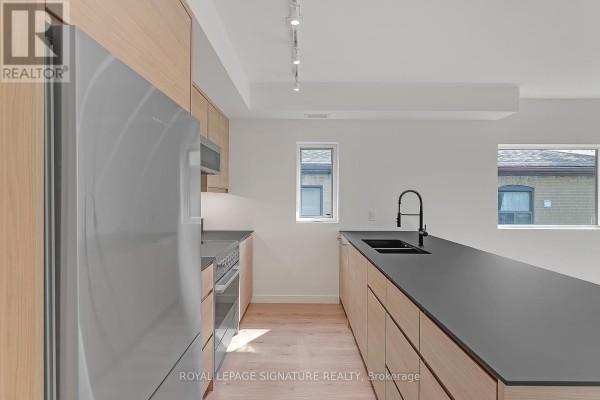 Kitchen area with light wood cabinets, stainless steel refrigerator, and black countertop island. - 4 - 1254 Davenport Road, Toronto