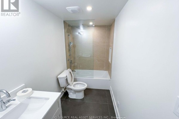 Bathroom with a toilet, sink, and bathtub/shower combination with beige tile surround. - 4 - 150 Brunswick Avenue, Toronto