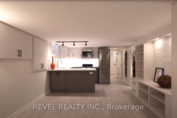 Basement living area and kitchen with light wood floors, white brick accent wall, and shelving. - 4 - 27 Glen Elm Avenue, Toronto