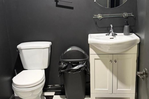 Powder room with a toilet, white vanity with sink, and trash bin against dark gray walls. - #4 - 5657 Hwy 7, Vaughan
