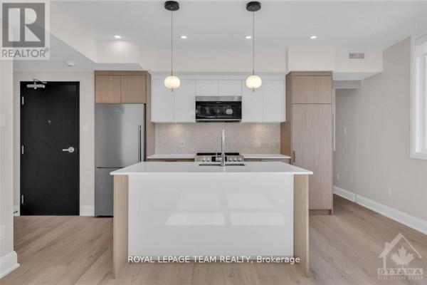 Open concept kitchen with island, stainless steel fridge, and white and wood cabinets. - 4 - 58 Florence Street, Ottawa