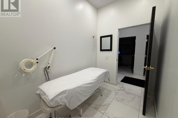 Treatment room featuring a massage table and magnifying lamp, with a doorway to another room. - 4 - Rm #3 - 5027 Hurontario Street, Mississauga