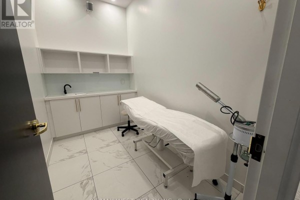 Spa room with a massage bed, steam machine, sink, and shelves. White tiled floor. - 4 - Rm #3 - 5027 Hurontario Street, Mississauga