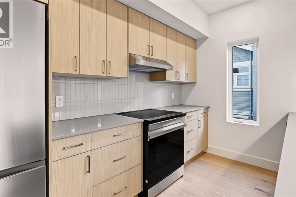 Bright living area with light wood floors, three vertical windows, and a view into a hallway. - 4 1721 Adanac St, Victoria