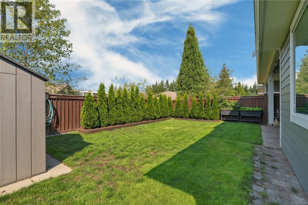 Covered patio overlooking a green backyard with a privacy fence of manicured evergreen trees and outdoor furniture. - 4 200 Nikola Rd, Campbell River